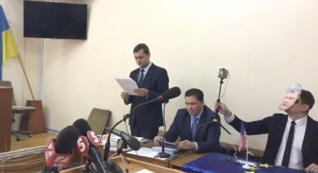Блогер Філімоненко в суді вдає з себе Порошенка. Перед ним прапор США, на столі -- прапор Євросоюзу