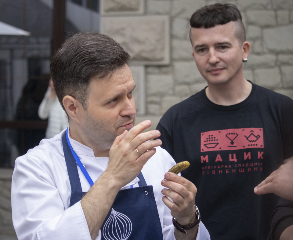 Польський кухар готує одну зі своїх автентичних страв. Фестиваль "Мацик" у Рівному. Ведучий свята Міцик Гонібес, у чорній футболці, уважно слухає. Фото -Радіо Трек. 