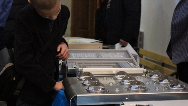 Молодий учасник форуму розглядає предмети на виставці енергозберігаючих технологій. На цьому столі - світлильники.